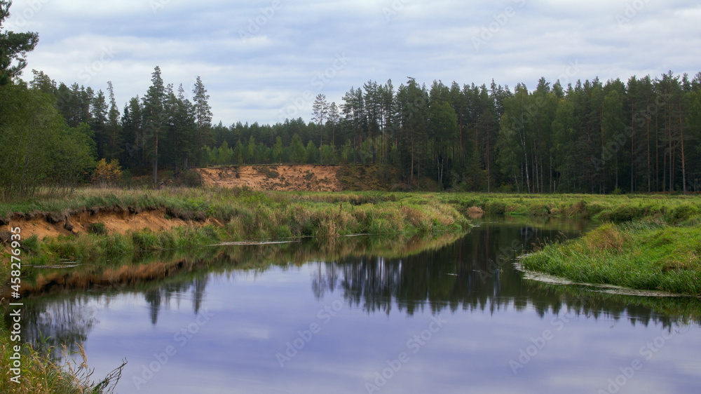 a small river with steep sandy banks flows in the forest against the background of an autumn forest