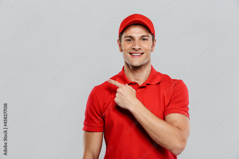 Young delivery man wearing uniform smiling and pointing finger aside Young delivery man wearing uniform smiling and pointing finger aside
