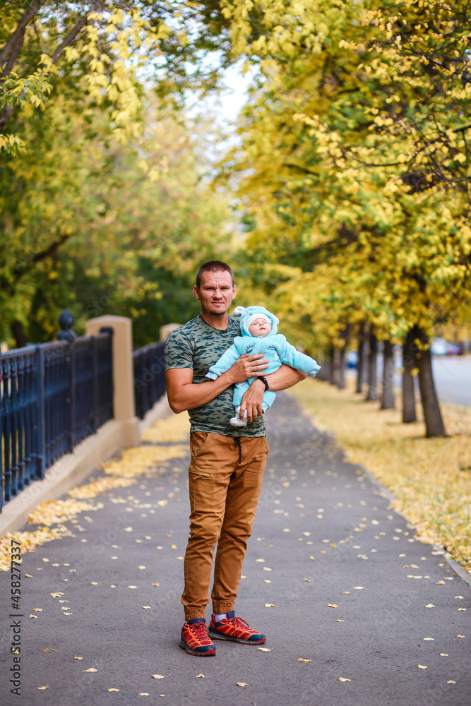 muscular man in brown pants and a newborn baby in her arms in the fall