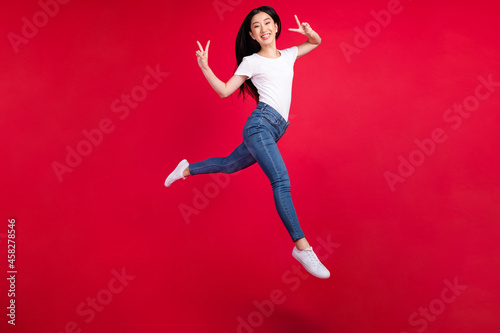 Full size profile side photo of young korean girl happy smile run go jump show victory v-sign isolated over red color background