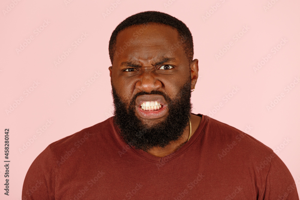 Aggressive bearded Afro-American guy model in brown t-shirt grimaces posing for camera on pink background in studio closeup Aggressive bearded Afro-American guy model in brown t-shirt grimaces posing for camera on pink background in studio closeup
