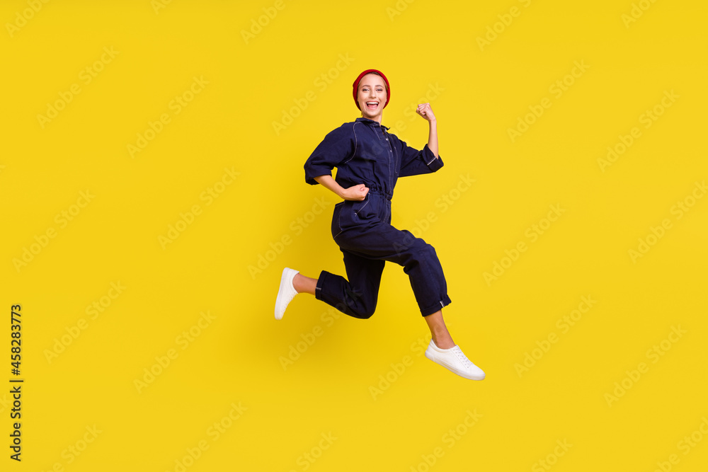 Full size photo of young beautiful smiling woman running fast speed in air wear red beanie isolated on yellow color background