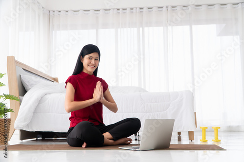 Portrait of healthy young Asian woman practicing yoga exercises sitting in the bedroom and learning online on laptop at home. Concept of exercise and relaxation, Technology for New normal lifestyle