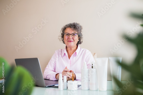 Satisfied businesswoman with assorted cosmetic products against laptop in office