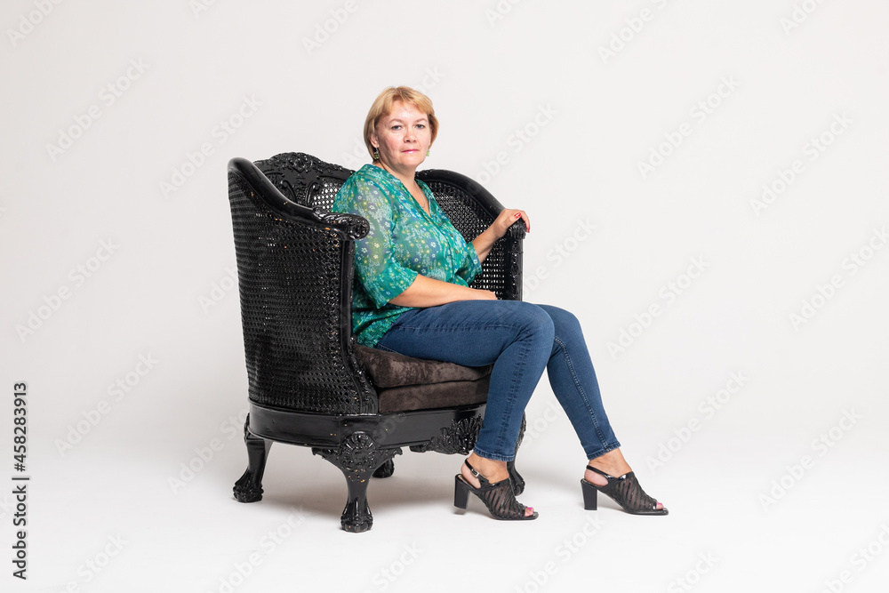 Mature woman smiling and sitting in an armchair isolated on white background