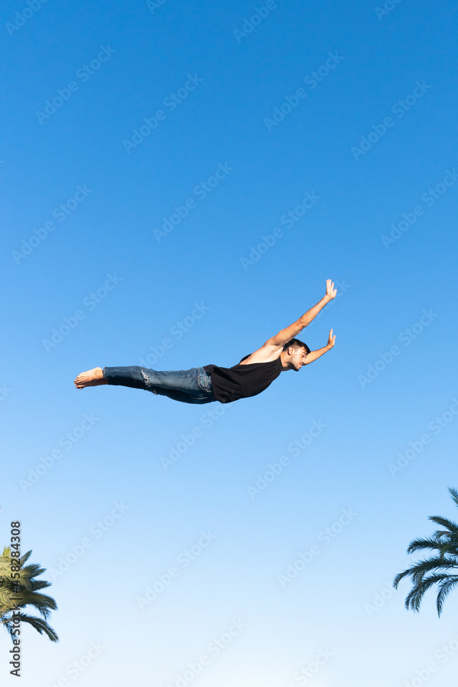 Energetic dancer performing trick in mid air above palm trees Energetic dancer performing trick in mid air above palm trees