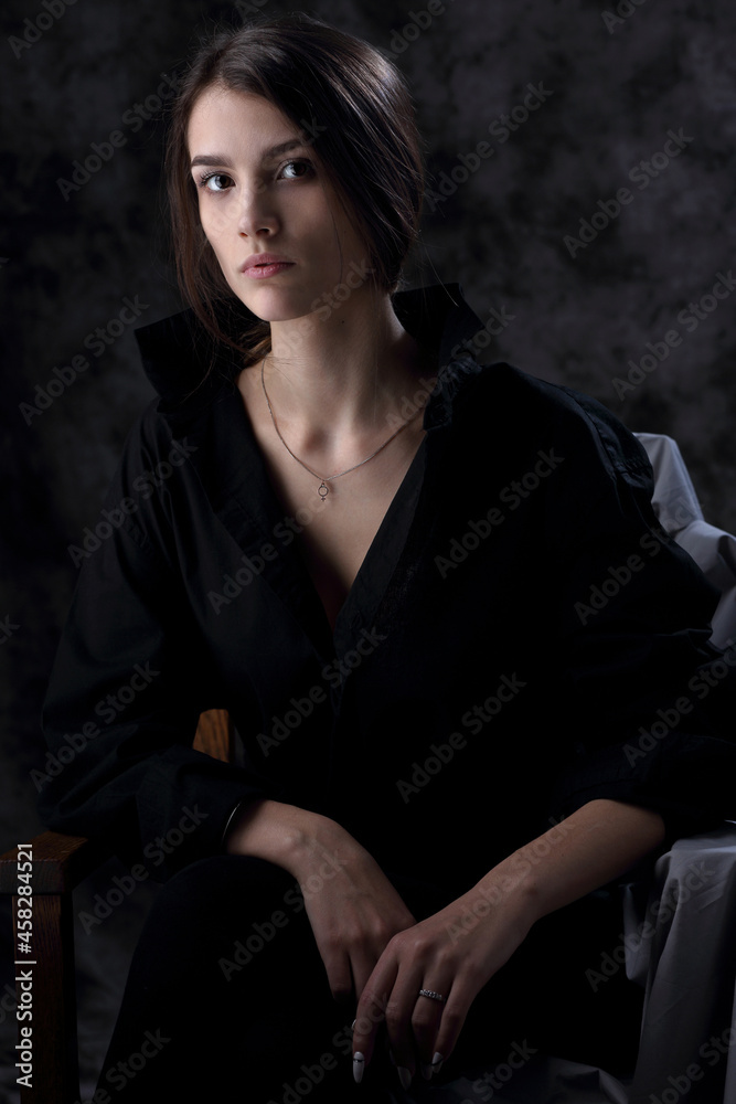 Portrait of a beautiful girl in a black men's shirt on a dark background Portrait of a beautiful girl in a black men's shirt on a dark background
