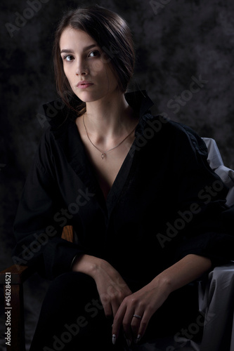 Portrait of a beautiful girl in a black men s shirt on a dark background