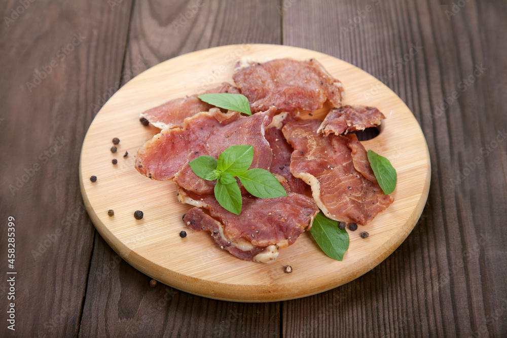 Pieces of jerky meat with basil leaves lie on a wooden cutting board on a wooden background. Pieces of jerky meat with basil leaves lie on a wooden cutting board on a wooden background.