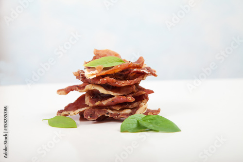 Pieces of jerky are in a pile, decorated with basil leaves on a white background.