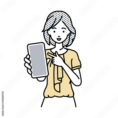 立ってスマートフォンを指差してこちらに向けて見せているオフィスカジュアルの女性