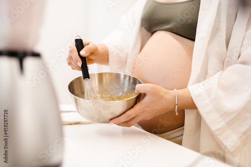 White pregnant woman whipping eggs in kitchen at home