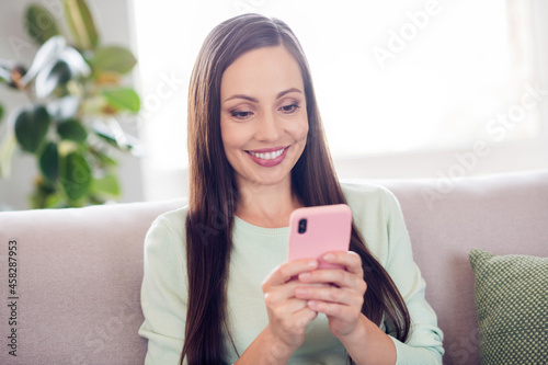 Photo of funky young brunette lady sit on sofa look telephone wear blue shirt at home alone