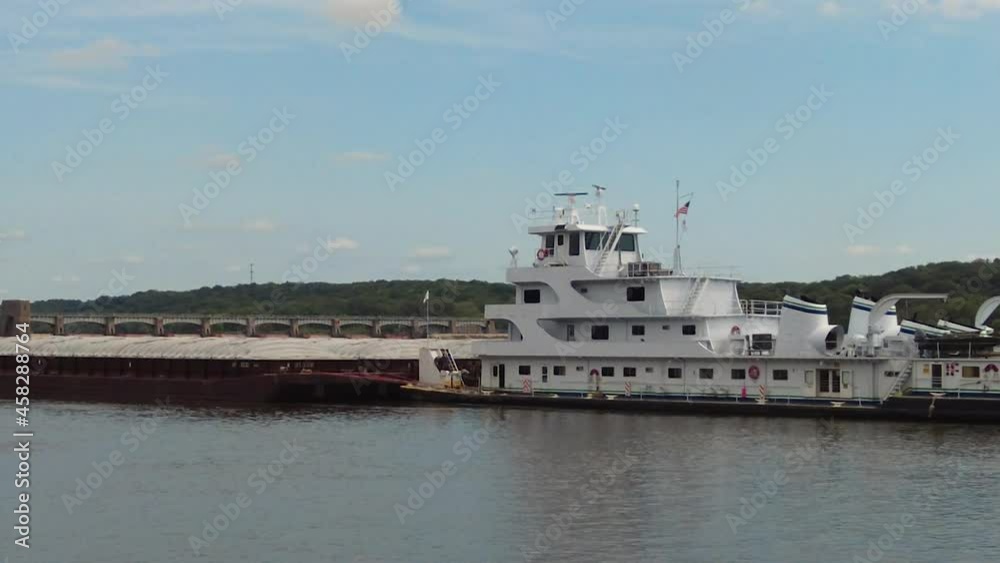 Zoom out view of pusher boat moving a barge slowly through Lock No. 14 on Upper Mississippi River; Interstate 80 Bridge over river in background; concepts of transportation and river life Zoom out view of pusher boat moving a barge slowly through Lock No. 14 on Upper Mississippi River; Interstate 80 Bridge over river in background; concepts of transportation and river life