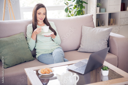 Photo of nice young brunette lady sit on sofa drink tea watch film wear blue shirt at home alone