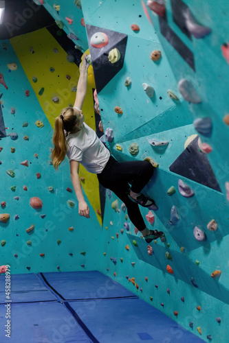 Smiling girl climbs the climbing wall, the woman is engaged in extreme sports, rock climbing in the city, strength and endurance training