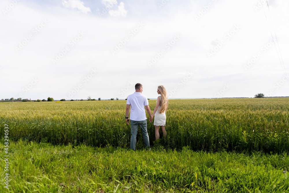 Rear view shot of a young woman walking with her boyfriend on a grass field. Couple enjoying a walk on the grassy ground.