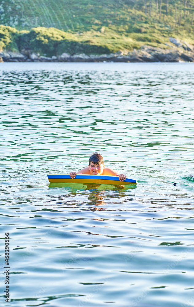 Happy child playing in the sea with bodyboard. Child having fun outdoors. Concept of summer vacation and healthy lifestyle