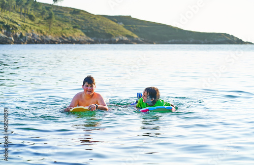 Happy children looking at camera playing in the sea with bodyboard. Children having fun outdoors. Concept of summer vacation and healthy lifestyle © Nedrofly