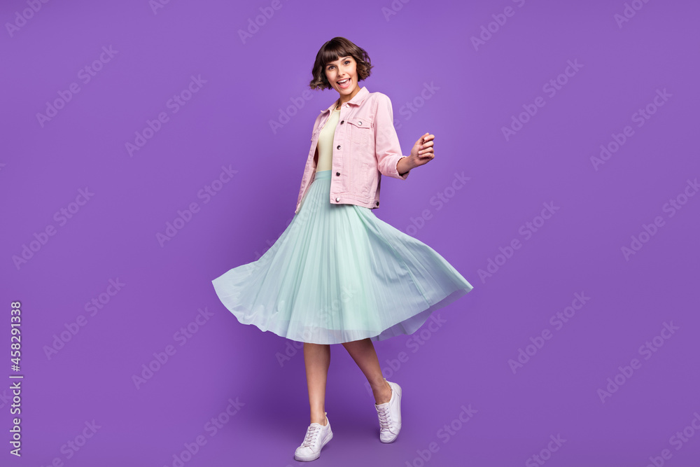 Full length photo of young pretty cheerful amazed woman wear skirt wind blow isolated on violet color background Full length photo of young pretty cheerful amazed woman wear skirt wind blow isolated on violet color background