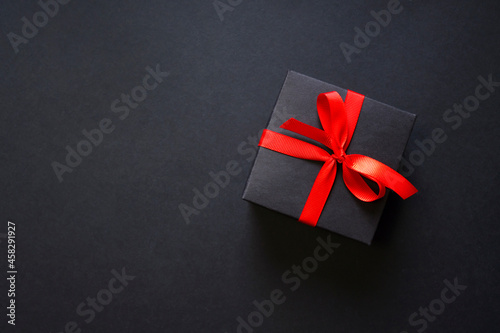 Black Friday elegant background with a black gift box and red bow ribbon. Top view. Composition with copy space.