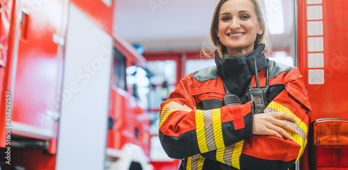 Fire fighter woman standing in front of a fire truck with her arms crossed photo