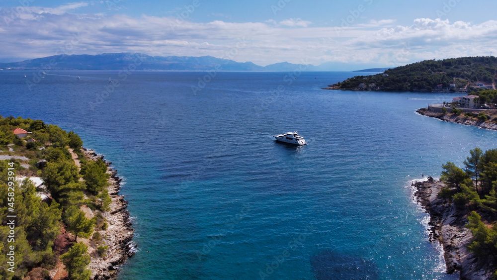 View of the sea coast and beach Kašjun on the island of Šolta. Yacht in a bay in the adriatic sea. Mountains in the background. Split city in the distance. Dalmatia. Croatia. Europe
