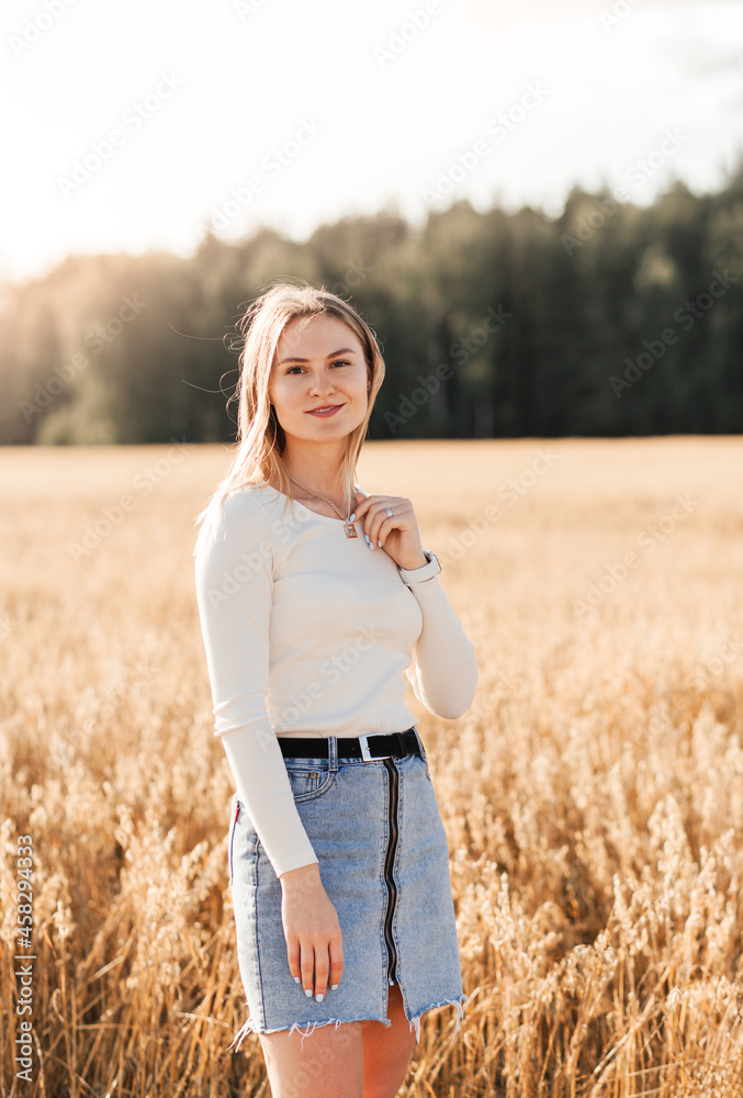 A young beautiful girl in a denim skirt walks through a wheat field on a sunny day A young beautiful girl in a denim skirt walks through a wheat field on a sunny day