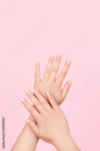 Female hands with beautiful manicure - pink nude nails on pink background. Nail care concept