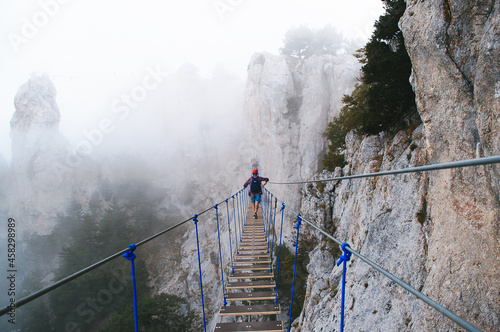 A young man in mountaineering equipment walks uphill on a suspension bridge in the fog.  Suspension bridge on Mount Ai-Petri, Yalta, Crimea. The concept of travel, active lifestyle, tourism.