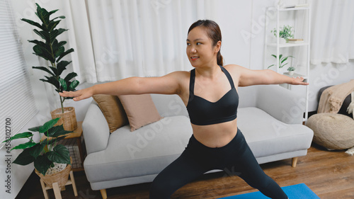 Portrait of gorgeous young asian woman practicing yoga at home stretching out while following a yoga routine