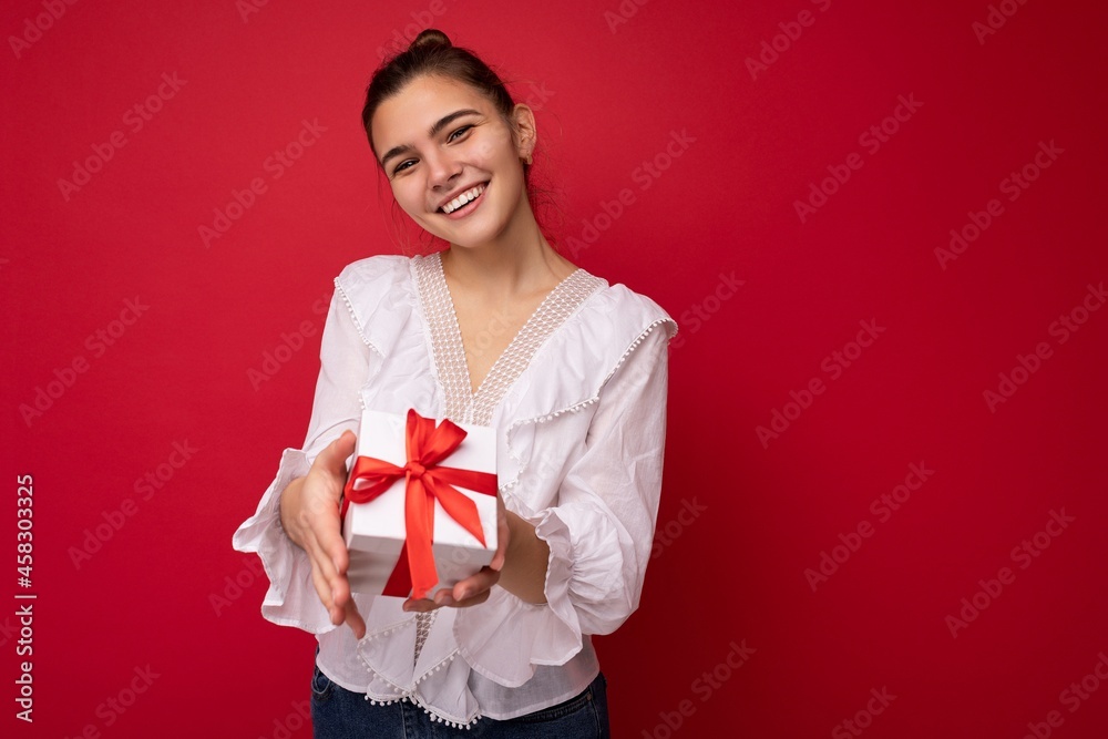 Beautiful happy young brunette woman isolated over colourful background wall wearing stylish casual clothes holding gift box and looking at camera Beautiful happy young brunette woman isolated over colourful background wall wearing stylish casual clothes holding gift box and looking at camera