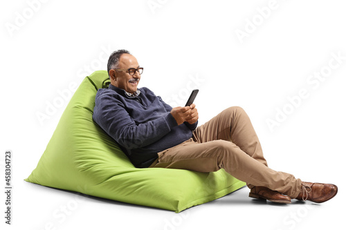 Mature man sitting on a green bean bag chair and using a mobile phone photo