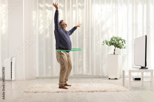 Full length profile shot of a mature man spinning a hula hoop in front of tv