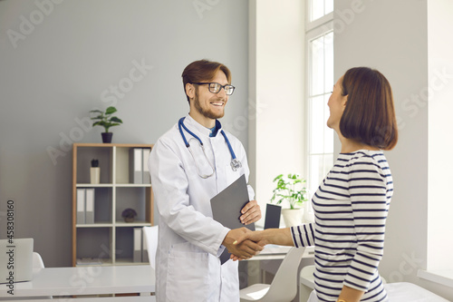 Health care in a hospital or private clinic. Smiling young male doctor shakes hands as sign of greeting and acquaintance with female patient at the hospital. Concept of doctor-patient relationship.