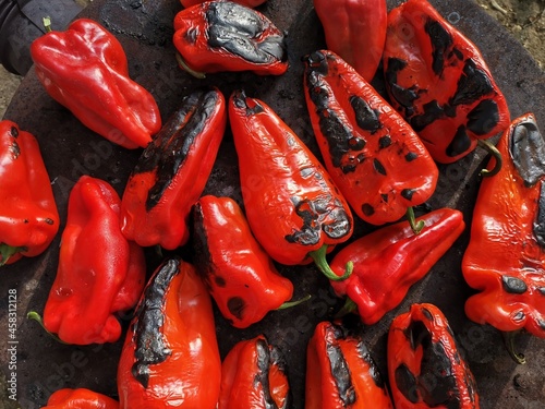 Roasting red peppers on wood burning stove. Close-Up of roasted red peppers on wood-heated stove. Baked red pepper on coal fire, rustic outdoor cooking. 