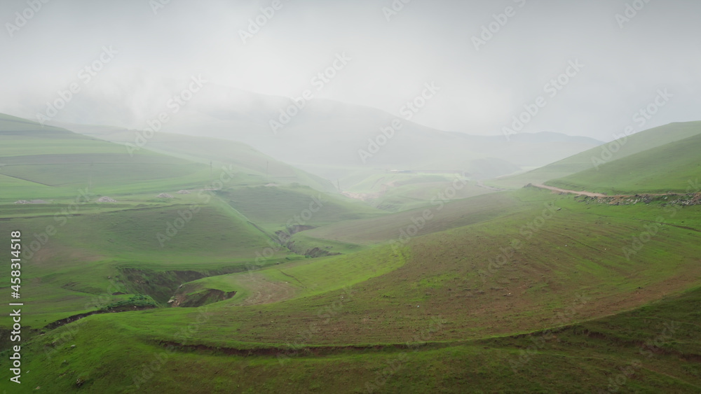 The copter's flight in the afternoon over a green gorge towards the hills and a cloudy rainy sky. A beautiful idyllic landscape with green fields, roads and hills on a cloudy day. Beautiful natural. The copter's flight in the afternoon over a green gorge towards the hills and a cloudy rainy sky. A beautiful idyllic landscape with green fields, roads and hills on a cloudy day. Beautiful natural.