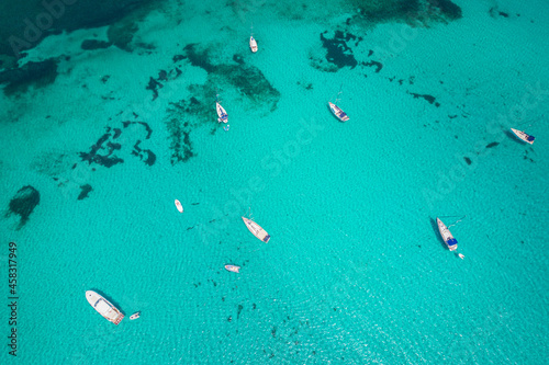 Aerial view of many yachts and sailboats in turquoise water in Mediterranean Sea next to Sardinia island, La Pelosa beach