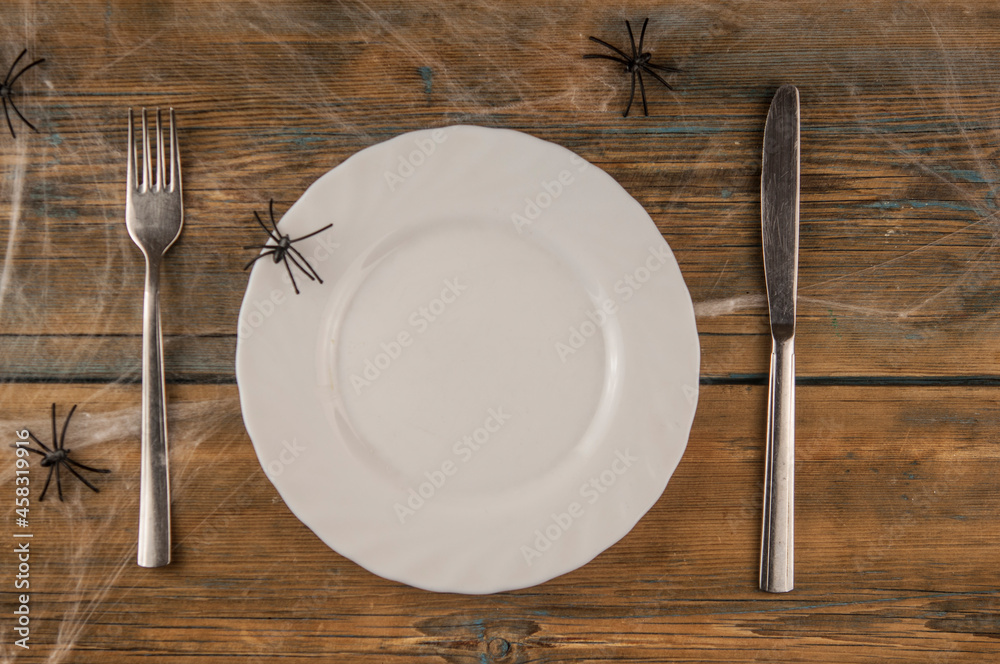 Halloween table setting blank dish, knife and fork with spider web on wood background. Flat lay, top view trendy holiday concept. Halloween table setting blank dish, knife and fork with spider web on wood background. Flat lay, top view trendy holiday concept.