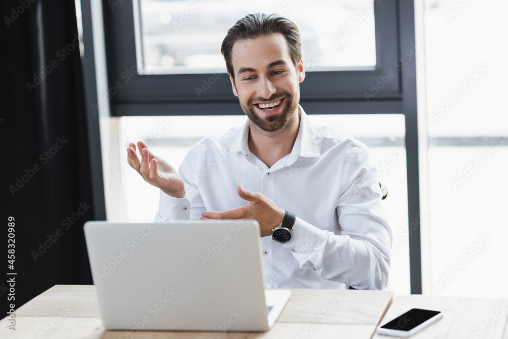 positive businessman pointing with hands near laptop and smartphone with blank screen in office positive businessman pointing with hands near laptop and smartphone with blank screen in office