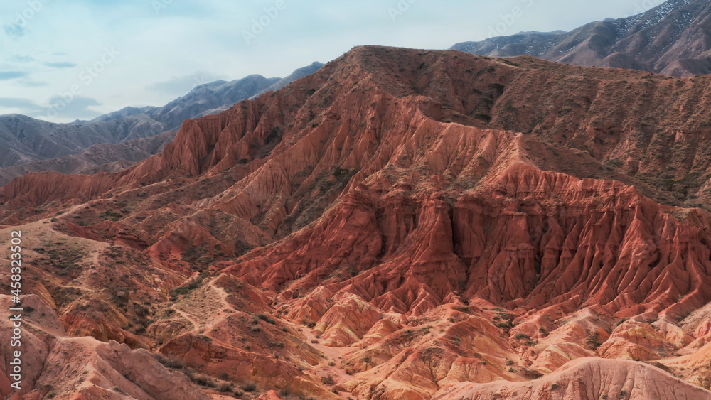 An unusual aerial landscape with huge red brown rocks and a mountain on which a man in a red T-shirt is sitting and meditating. A deserted canyon with gorges filmed on a copter on a sunny day. An unusual aerial landscape with huge red brown rocks and a mountain on which a man in a red T-shirt is sitting and meditating. A deserted canyon with gorges filmed on a copter on a sunny day.