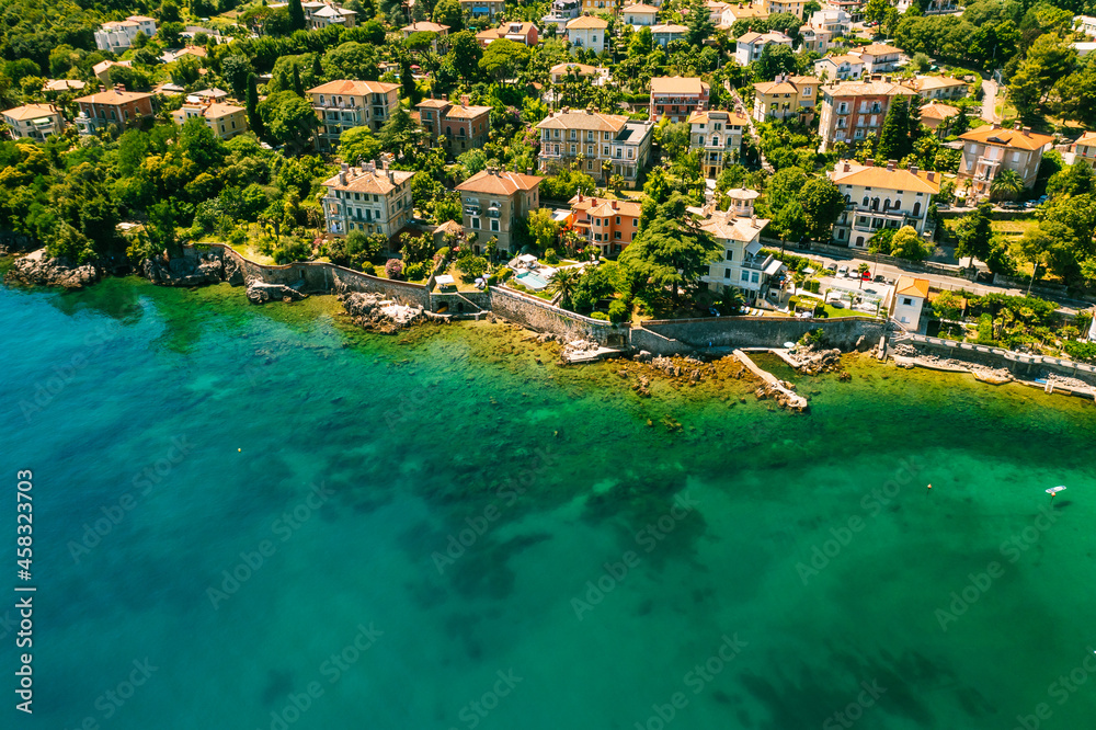 Beautiful villas near the coast of rocky beach in a small town Lovran, Croatia. Arial view of Lungomare sea walkway with transparent water. Beautiful villas near the coast of rocky beach in a small town Lovran, Croatia. Arial view of Lungomare sea walkway with transparent water.