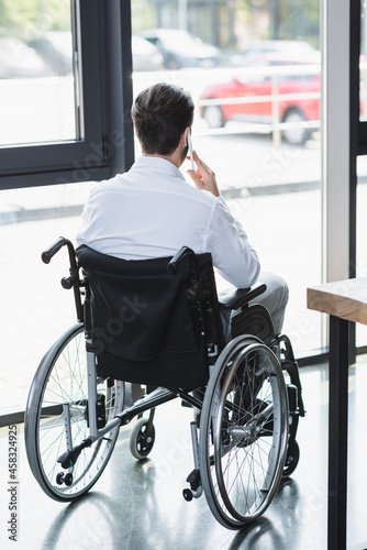 back view of disabled businessman in wheelchair talking on smartphone near window in office © LIGHTFIELD STUDIOS