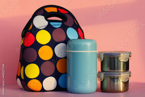 snack on a break with a lunchbox. colorful handbag, blue thermos and two metal containers with food. lunch for a schoolboy or an office worker.