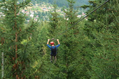 Man have a fun on zipline among the tops of firs.