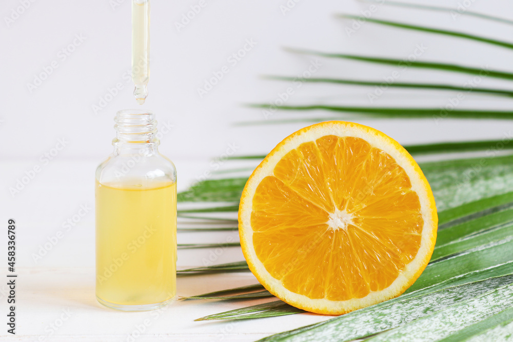Bottle of cosmetic skincare serum with dropper, orange and palm leaf. Citrus essential oil with Vitamin C. Serum is dripping from dropper. Selective focus. Beauty and spa concept Bottle of cosmetic skincare serum with dropper, orange and palm leaf. Citrus essential oil with Vitamin C. Serum is dripping from dropper. Selective focus. Beauty and spa concept