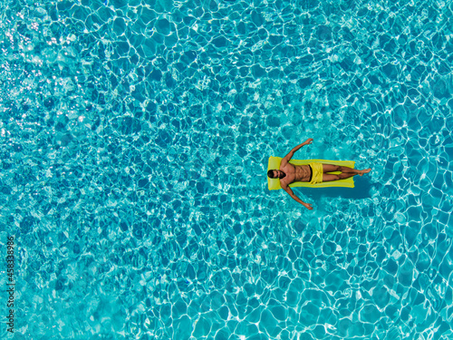 Vacation mood. Refreshment at the outdoor private pool on a sunny summer day. A man on a mattress in a pool. Aerial shot of a half-naked man floating on a mattress in a private resort