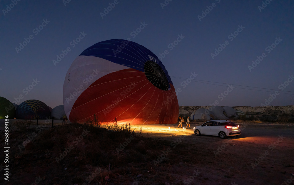 Obraz premium A car parked in front of a hot air balloon with headlights on during night, preparation of a flight in Goreme national park in Cappadocia, Turkey