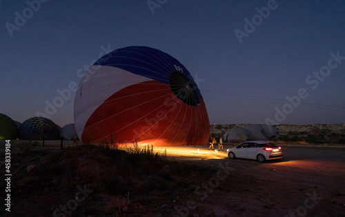 A car parked in front of a hot air balloon with headlights on during night, preparation of a flight in Goreme national park in Cappadocia, Turkey