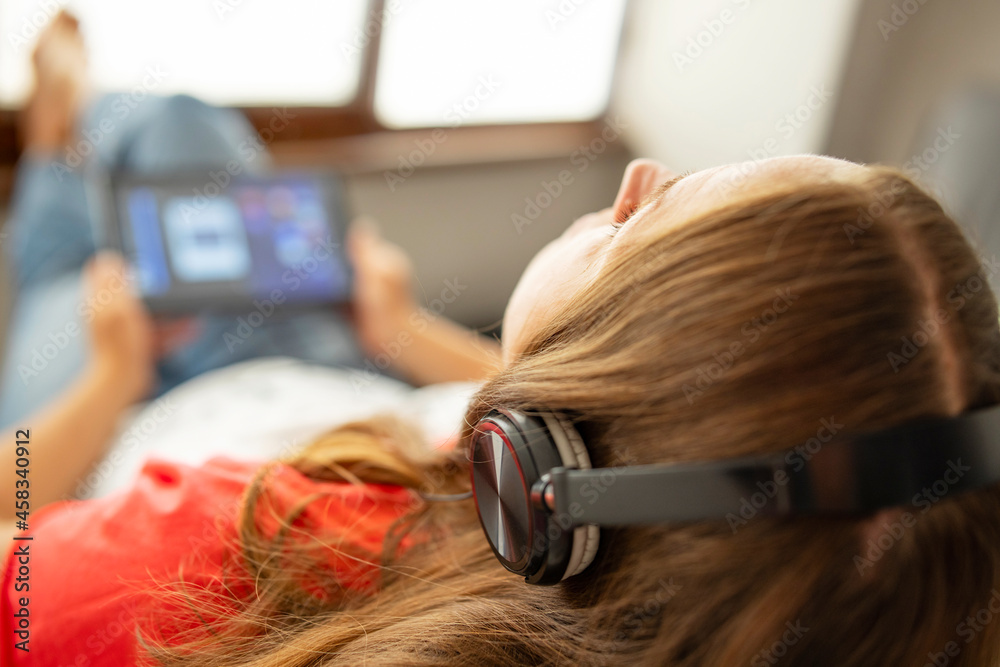 Fototapeta premium Young beautiful woman sitting in armchair near a window and listening to music using headphones. Happy calm woman in earphones rest on cozy armchair at home , stress free concept